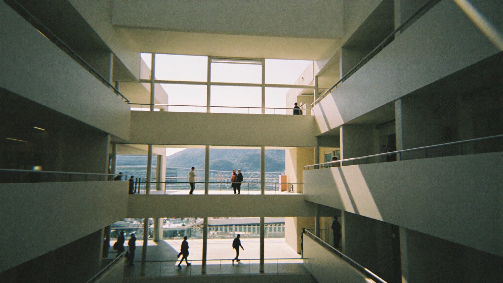 A bright office atrium seen from a mezzanine, a few small figures far below