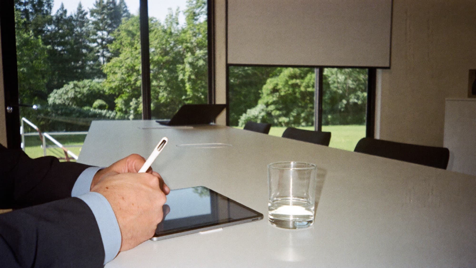 A hand signing on a tablet with a stylus in a glass meeting room