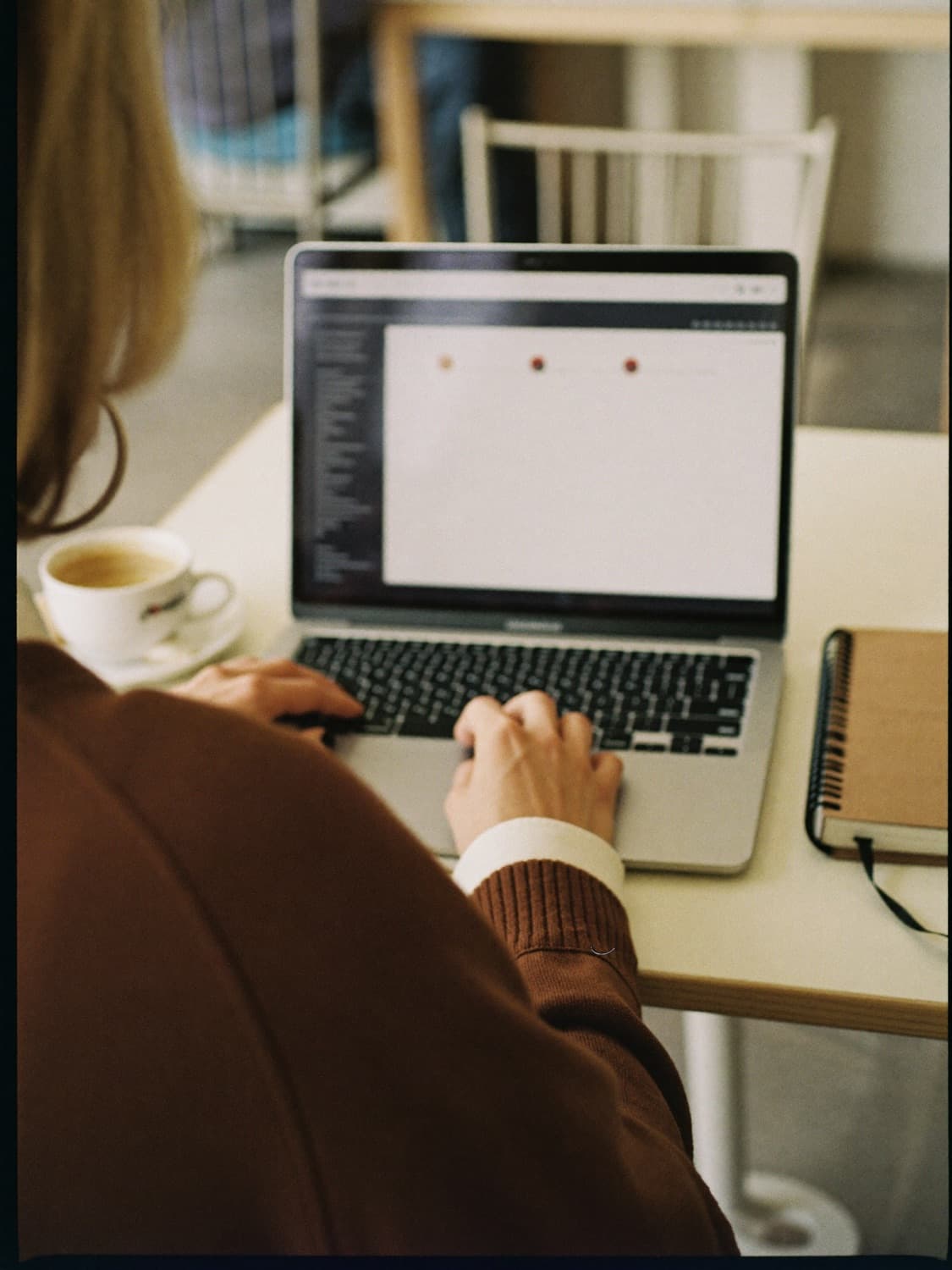 Someone writing an email on a laptop in a cafe, seen from behind