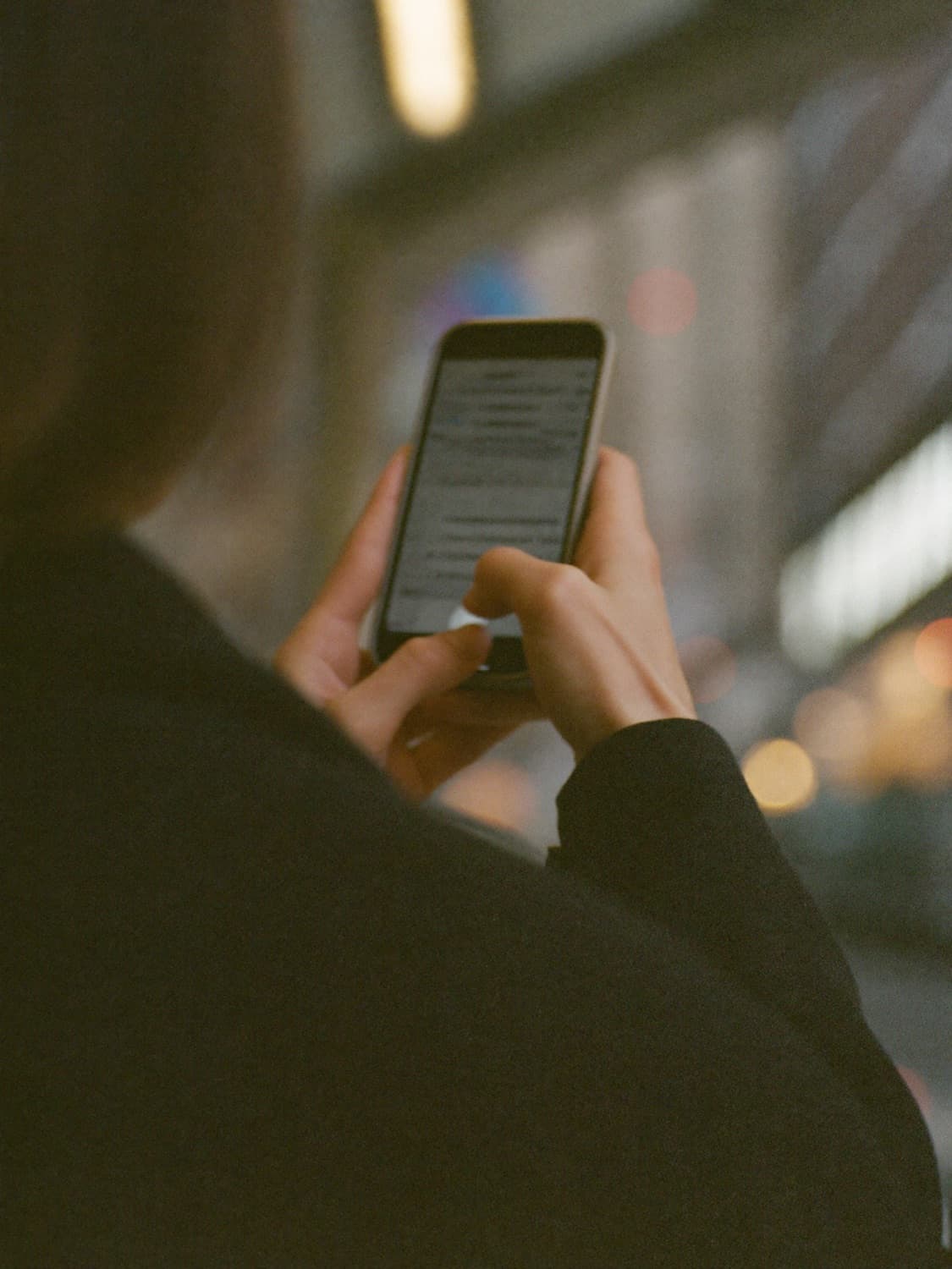 Over the shoulder of someone checking a phone at a bus stop, screen out of focus